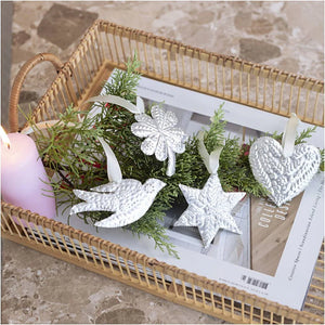 Decorative white ornaments on greenery with a candle in a woven basket.