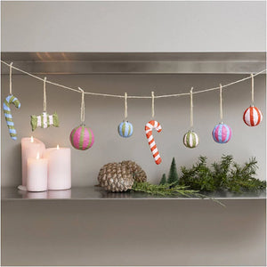 Decorative string with Christmas ornaments hanging above a shelf with candles and greenery.