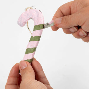 Hand holding a candy cane-shaped modelled from pulp with pink and green stripes against a white background