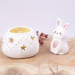 White ceramic rabbit and star-patterned container on a wooden surface with a light purple background