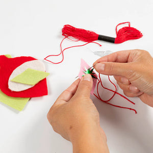 Person sewing a felt decoration with red thread on a white background