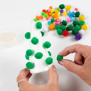 Person decorating a foam Christmas tree shape with colorful pom-poms on a white background
