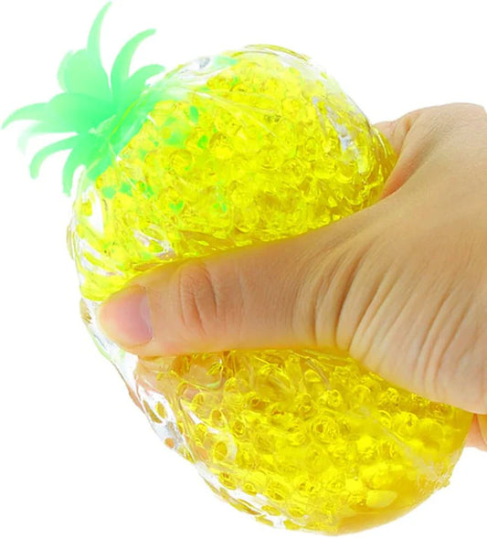 Yellow pineapple-shaped squishy toy being held by a hand on a white background