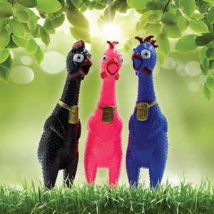 Three colorful bird-shaped toys in black, pink, and blue standing on grass with a green leafy background.