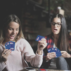 Three women playing a card game with blue cards in a casual setting.