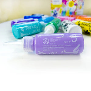 safety warning advising suitable for ages 3 years and up andon a purple coloured poster paint tube with the bottle laying on it's side on a white table with other paints in the background