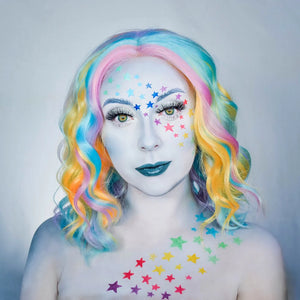 Person with colorful hair and snazaroo face paint featuring stars on a plain background