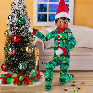 An elf scout decorating a christmas tree with lights while wearing the chrismtas tree themed Elf on a Shelf pyjamas