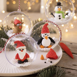 Christmas-themed decorations including Santa Claus, penguin, and snowman figures inside clear baubles on a wooden surface.