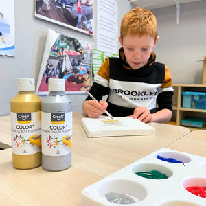 Child painting with Creall paint bottles and a color chart on a table.