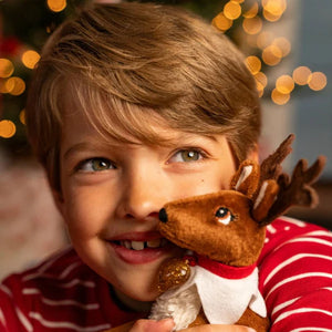 Child holding an Elf Pet reindeer plush toy with blurred Christmas lights in the background