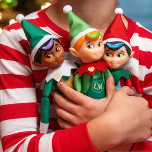 Three elf figurines held by a person wearing a red and white striped shirt.