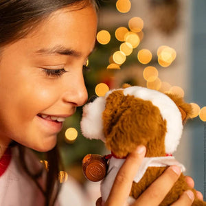 A girl touching her nose to the Elf Pet Saint Bernard plush toy with a christmas tree sparkling in the background