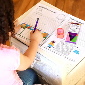 Child writing in a workbook with educational materials on a wooden surface