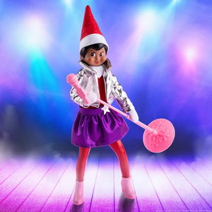 A scout elf wearing the MagiFreez - Polar Pop Star outfit set with silver jacket, red leggings, purple skirt, pink microphone, and pink high heels on a blue and purple background.