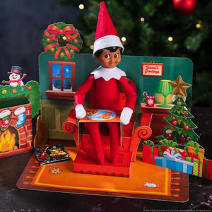 An elf scout sitting on a pop up armchair in a sitting room decorated for Christmas from The Elf on the Shelf 20th Anniversary - Pop Ups set