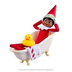 Elf on the Shelf figurine in a bathtub with a rubber duck and towel on a white background