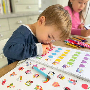 Child coloring in a book with colorful pencils on a table.