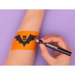 Person applying a bat-themed temporary tattoo with a Snazaroo marker on a purple background