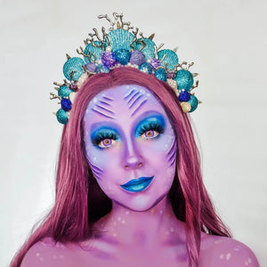 Person with purple snazaroo face paint and makeup with a decorative headpiece on a plain background